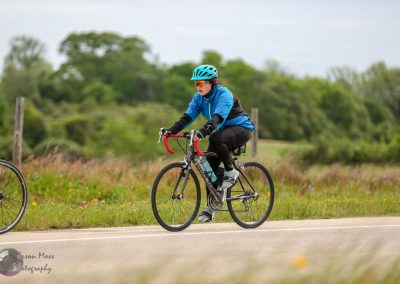 Cyclist riding a bicycle along a scenic trail with greenery in the background, representing Bluebonnet Express.