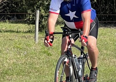 Vibrant cyclist in patriotic Texas-themed jersey on a road bike riding outdoors during daytime.