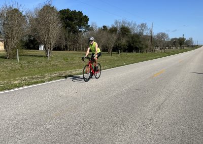 Vibrant cyclist riding a red bike on a scenic rural road under a bright blue sky.