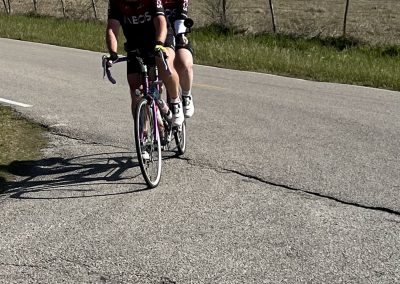 Bright red Bluebonnet Express cycling team jerseys, two riders on a scenic rural route, enjoying outdoor recreation.