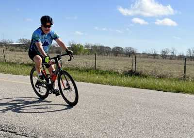Cyclist riding on a rural road during daytime, promoting Bluebonnet Express cycling event.