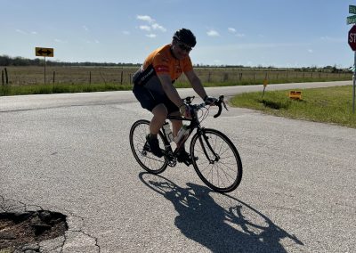 Cyclist riding a bike on rural road, outdoors, sunny day, Bluebonnet Express.