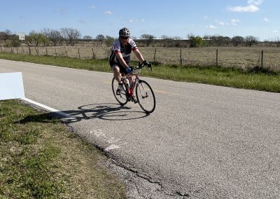 Bicycle rider on a rural road during daytime, promoting Bluebonnet Express cycling events and scenic bike routes.