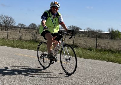 Vibrant cyclist riding on scenic open road with blue sky and countryside background.