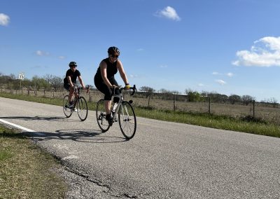 Cyclists riding on open road with blue sky and scenic landscape, Bluebonnet Express biking adventure.