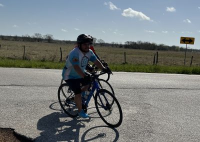 Riding a bicycle on a rural road with open fields and a clear blue sky.