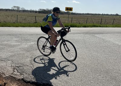 Cyclist riding on a rural road with Bluebonnet Express branding in the background.