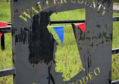 Old metal sign with "Waller County Fair & Rodeo" text, silhouette of a cowboy, outdoors, rainy weather.