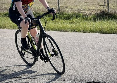 Bright cyclist wearing a colorful jersey and neon yellow helmet riding a bike on a rural road.