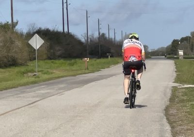 Gentleman riding a bicycle on a rural road surrounded by nature and utility poles, promoting outdoor cycling and eco-friendly transportation.