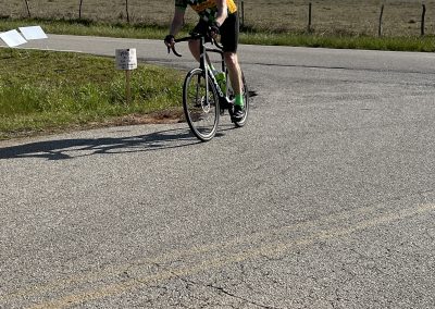 Cyclist riding a bike on rural road during daytime under blue sky with clouds.