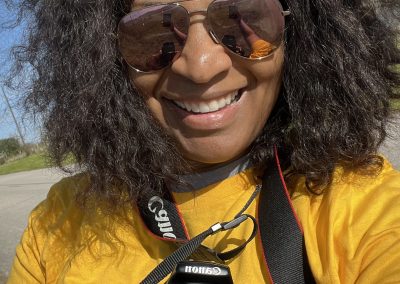 Colorful cyclist wearing sunglasses and yellow jersey, holding a camera outdoors.
