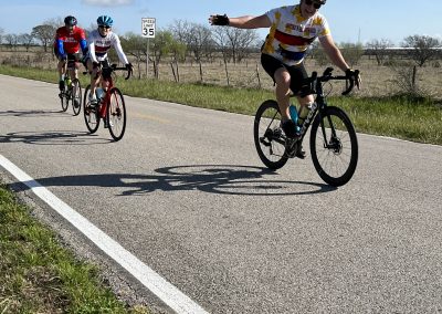Group of cyclists riding on scenic Texas highway during daytime, promoting Bluebonnet Express bike event.