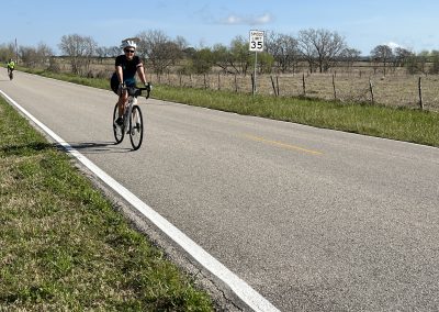 Cyclist riding on rural road with bluebonnet express sign in background, spring scenery, Texas.