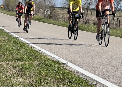 Cyclists riding along a rural road in a scenic outdoor setting.
