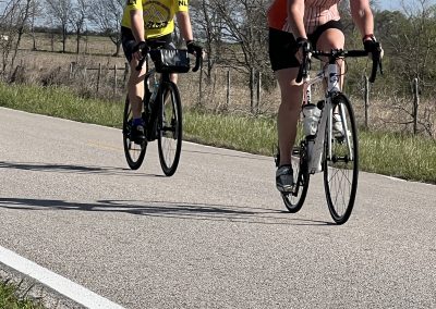 Vibrant cyclists riding on scenic rural road with blue sky, promoting Bluebonnet Express bicycle tours and healthy outdoor activity.