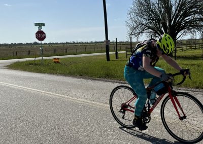 Bright cyclist wearing a yellow helmet riding a red bicycle along a rural road with scenic landscape.