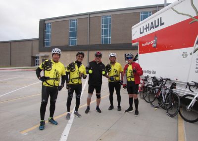 Cyclists in yellow jerseys with Bluebonnet Express support, near U-Haul truck, ready for cycling ride or event.