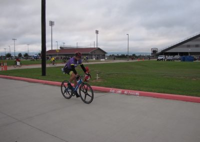 Bike rider on a blue bicycle at Bluebonnet Express event, outdoor cycling activity, overcast sky, stadium in background.
