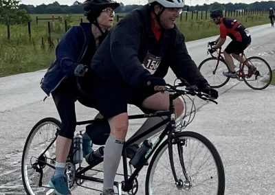 - Two cyclists riding on a scenic country road during daytime, wearing helmets for safety.