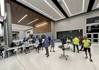 Bright indoor event space with participants, registration tables, and volunteers, promoting community and engagement.
