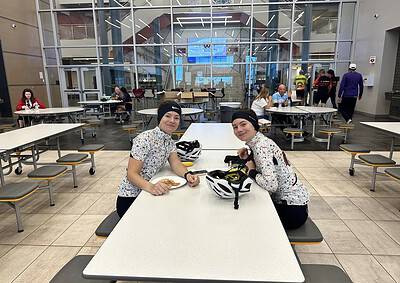 Bright indoor cafeteria where two cyclists, in cycling gear, enjoy a meal after a ride, with helmets on the table, showcasing active lifestyle and bike commuting.