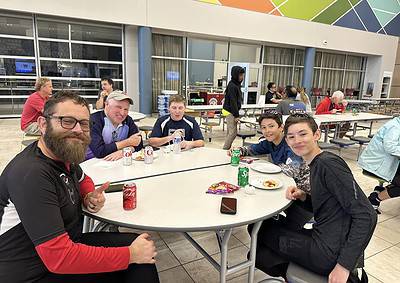 A group of kids and adults enjoying a meal at a cafeteria, with "Bluebonnet Express" signage visible in the background.