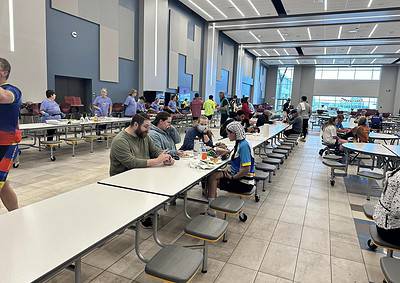 Bike travel station cafeteria with travelers enjoying meals at long tables, modern interior, bright lighting, and large windows.