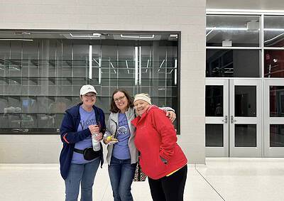 Joyful women volunteers at Bluebonnet Express event in casual attire, inside a modern building with glass and brick walls.