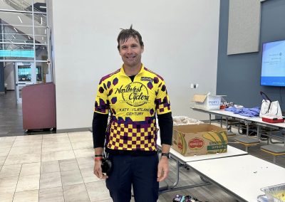 Bright smiling cyclist in NorthWest Cyclery jersey at Bluebonnet Express event, indoor location.
