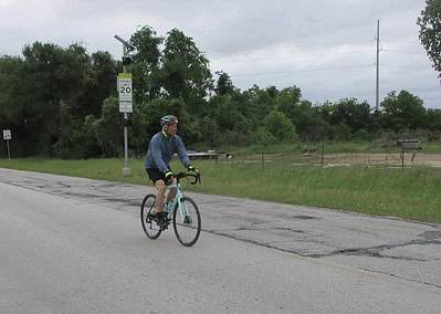 Cyclist riding on rural road near Bluebonnet Express, outdoor biking adventure, Texas scenery, safety gear.