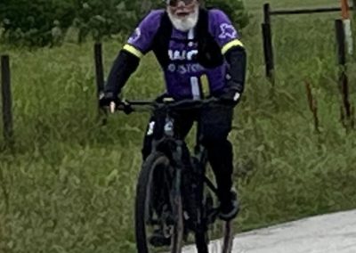 Vibrant cyclist riding mountain bike on trail with scenic greenery in the background.