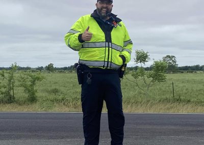 High-visibility police officer on roadside, smiling, giving thumbs-up, supporting Bluebonnet Express.