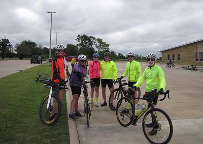 Brightly dressed cyclists with helmets and bikes gathered outdoors for a group ride event.