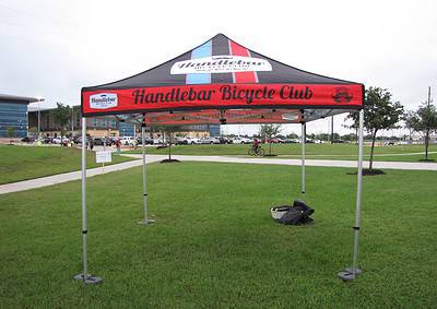 Bright red and black Handlebar Bicycle Club event tent in a grassy park setting.