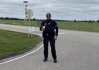Police officer with a coffee, standing on a rural road in Texas, promoting Bluebonnet Express bike service.