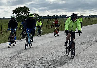 Group of cyclists riding on rural road in overcast weather, promoting Bluebonnet Express biking tours.