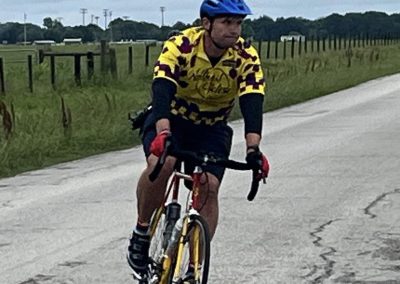 Vibrant cyclist in Bluebonnet Express jersey riding on scenic outdoor trail with rural background.