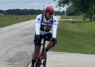 Bright cyclist riding on paved trail with greenery, overcast sky, and water tower in background.