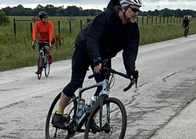 Men cycling on rural road with scenic countryside, bluebonnet express bike ride adventure.