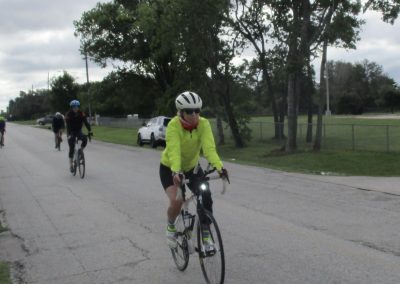 Bright yellow cyclist riding on a paved road during Bluebonnet Express event, with other cyclists in the background.