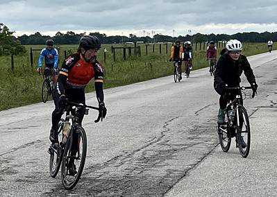 Cyclists enjoying a ride on scenic rural roads with grassy fields and cloudy skies behind them.