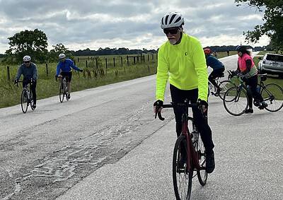 Bright neon yellow cycling jacket worn by man riding a bike with a group of cyclists on country road.