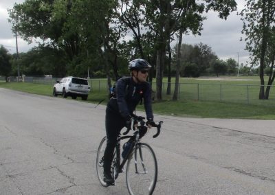 Cyclist riding a road bike during daytime on a paved street with trees and overcast sky.