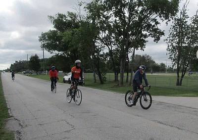 Bicycle riders enjoying a ride on a scenic outdoor bike trail during overcast weather.