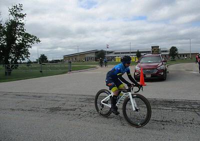 Cyclist riding on the road during Bluebonnet Express event with a school building in the background.