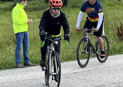 Bike race at Bluebonnet Express event with cyclists on the road, wearing helmets and biking gear, surrounded by greenery.