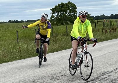 Bright yellow and neon cycling jackets on two cyclists riding on a rural road during daytime.
