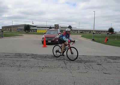 Cyclist participating in Bluebonnet Express bike race near school campus, supported by traffic cones.