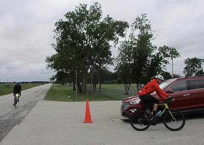Bright bluebonnet express bike event with cyclists riding near parked car and orange cone.
